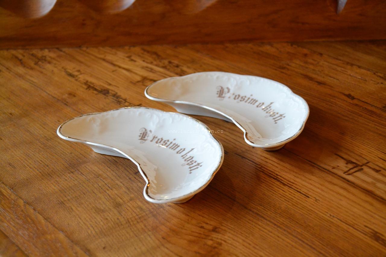 Porcelánové talířky ve tvaru rohlíku ozdobené nápisem „Prosím o kosti“
