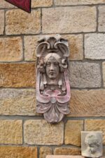 Secesní fasádní štukatérský reliéf s hlavou ženy a florálně ornamentálním dekorem.
