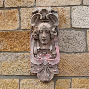 Secesní fasádní štukatérský reliéf s hlavou ženy a florálně ornamentálním dekorem.