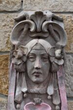 Secesní fasádní štukatérský reliéf s hlavou ženy a florálně ornamentálním dekorem.
