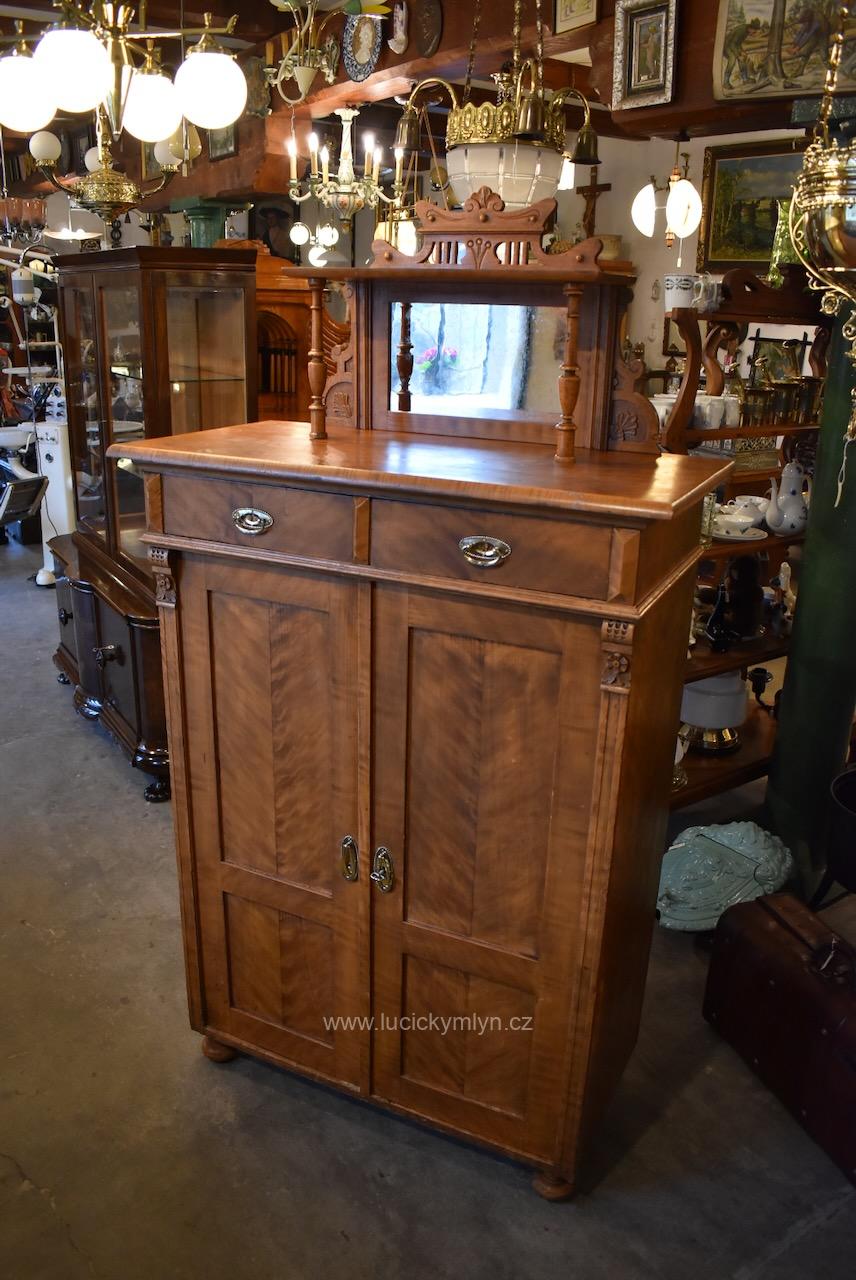 Vysoká starožitná secesní úložně dekorativní skříňka zvaná vertiko, truhlářsky vyrobená z měkkého dřeva, opatřená dobře zachovalým a světlým fládrovaným povrchem, jež věrně napodobuje skládanou dýhu obvyklou spíše na měšťanském nábytku Starožitná secesní skříňka vertiko s fládrovaným povrchem a zrcadlovou nástavbou