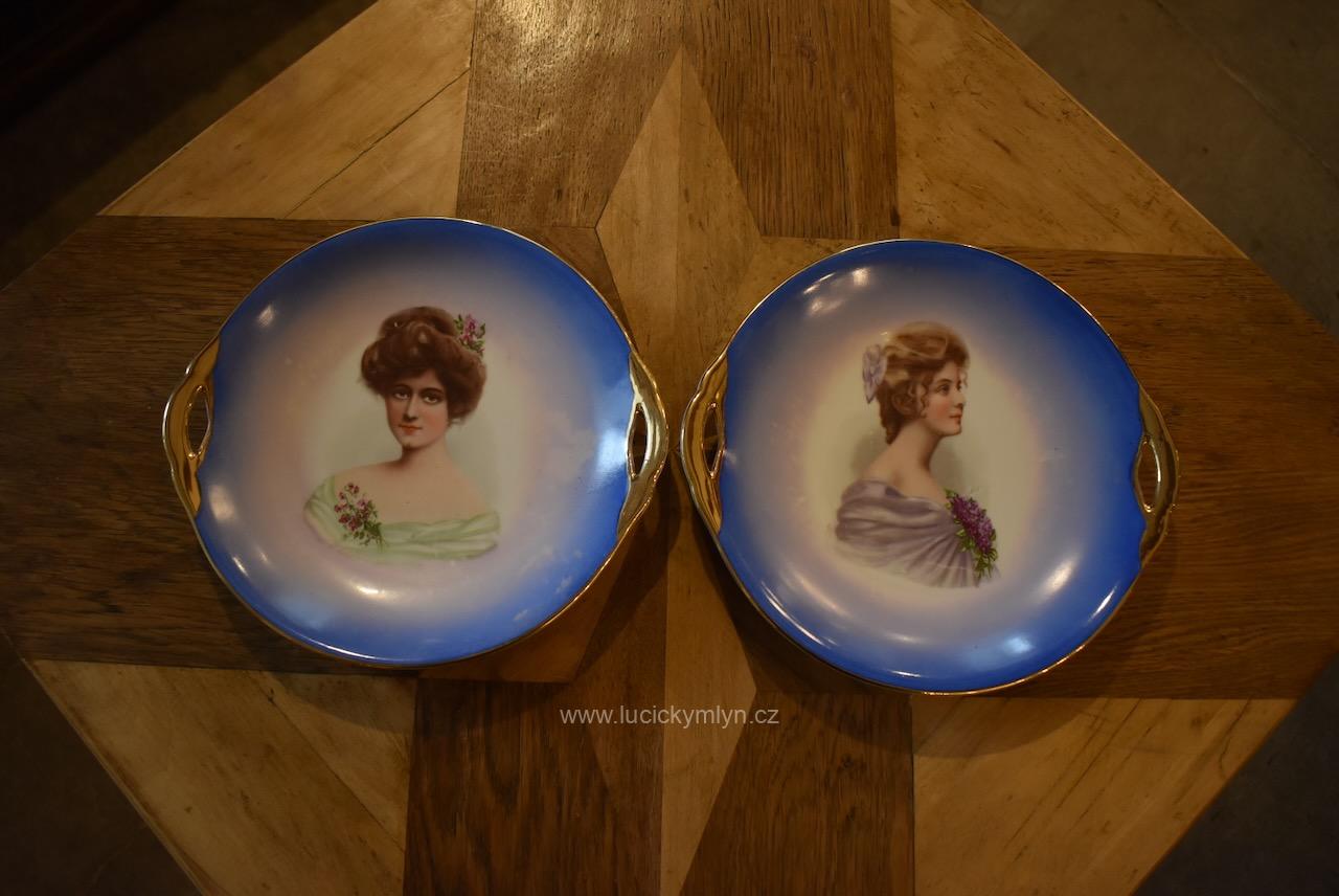 Starožitné secesní porcelánové talíře nejen pro sváteční servírování - měšťanský dekorativní porcelán působivě ozdobený kolorovanými portréty krásných dam i bohatým okrajovým zlacením s vykrojenými oušky Pár starožitných secesních porcelánových talířů s portréty dam a zlatými uchy.
