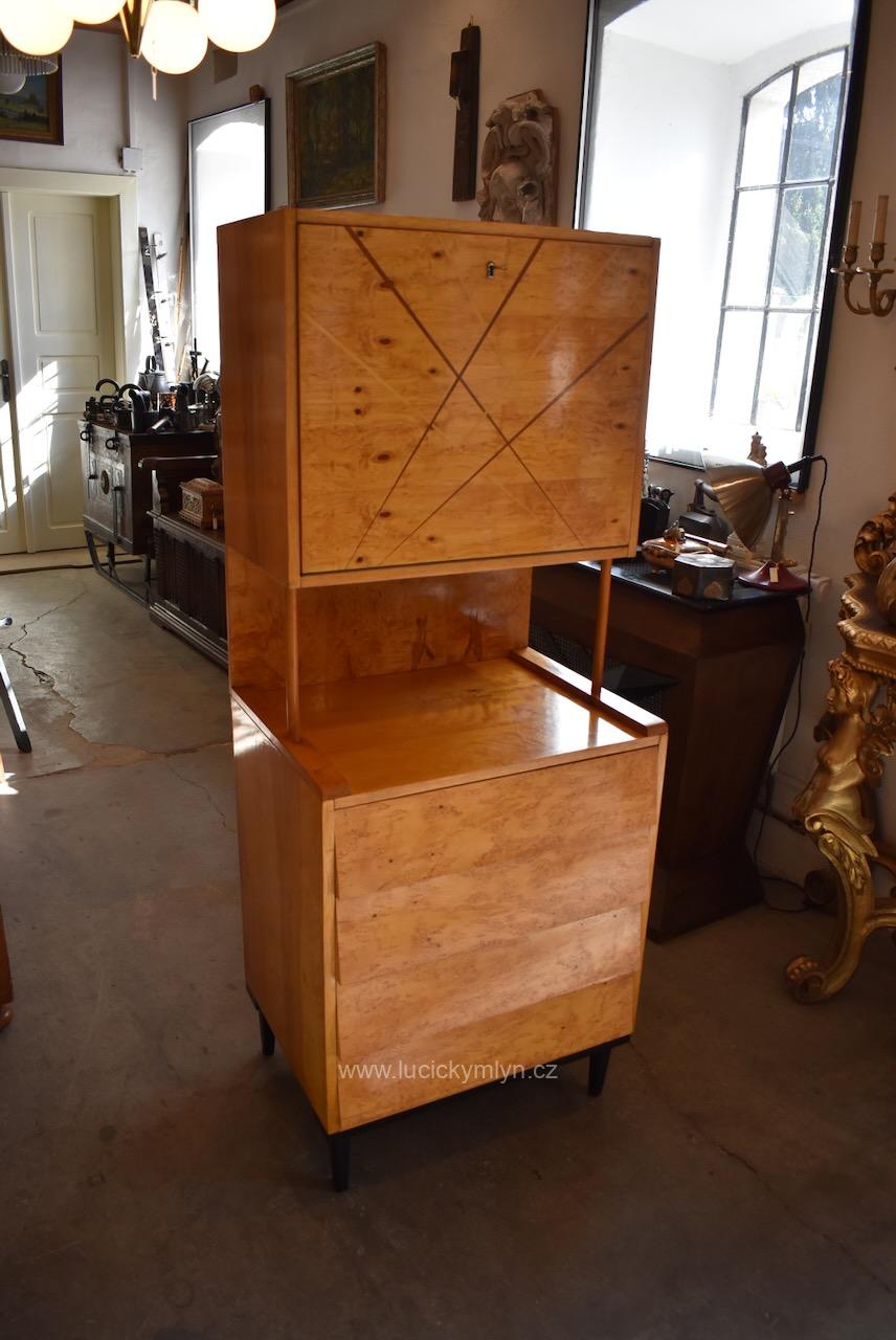 Hezký a zdařilý designový retro sekretář s šikovně výklopnou deskou modernisticky okrášlenou páskovou intarzií, pod meziprostorem je tento úzký nábytek opatřený čtyřmi praktickými zásuvkami, vše je dýhováno medově nazlátlou topolovou kořenicí (Kopírovat) Designový retro sekretář s výklopnou deskou a medovou topolovou kořenicí z období okolo roku 1970.