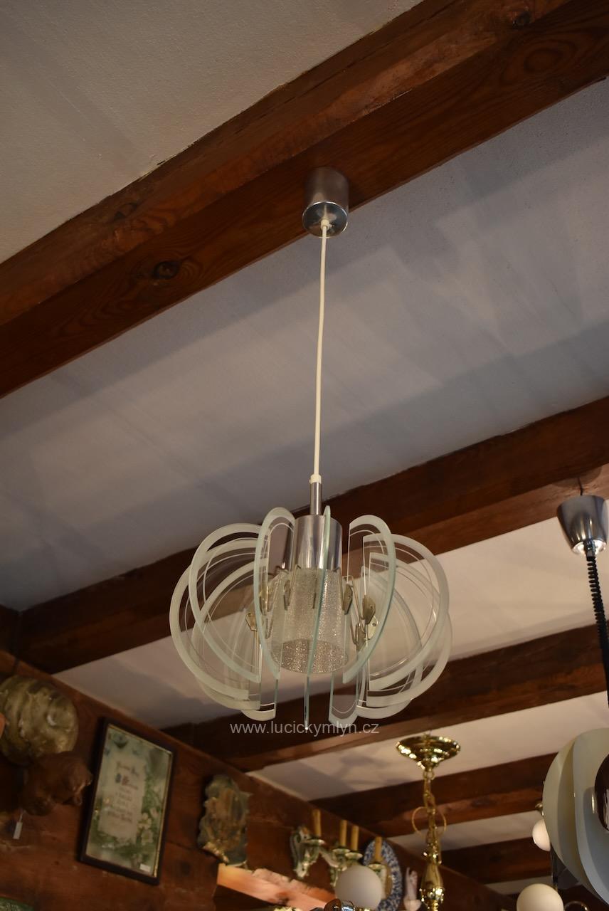 Zajímavý starožitný lustřík či závěsné světlo ztvárněné ve svěžím retro stylu jistě upoutá pozornost chromovaným válcovým centrálním dílcem zakončeným širším skleněným stínidlem jež hustě obklopují skleněné polokruhové disky či lamely Retro lustřík s chromovaným válcem a půlkruhovými skleněnými lamelami z 60.–70. let