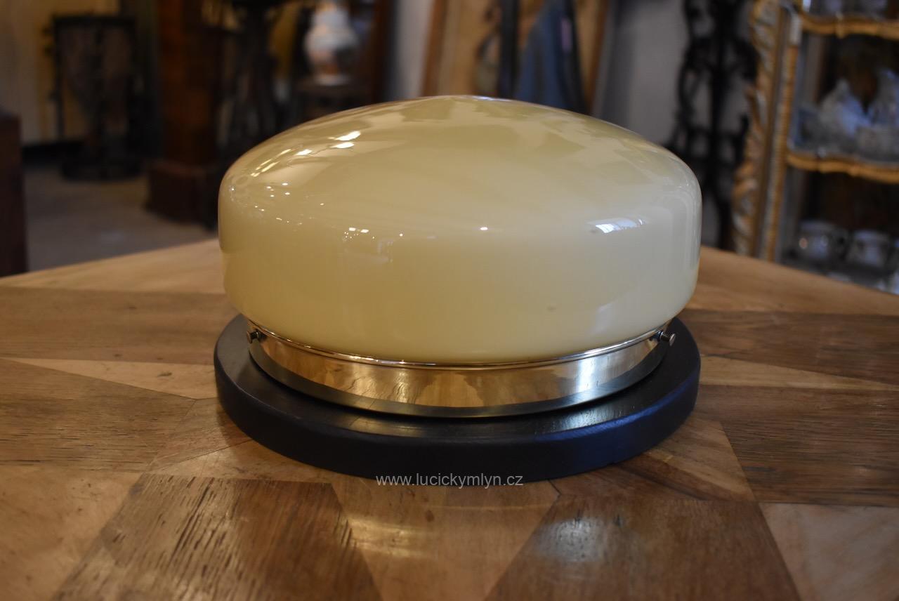 Středně velké a vkusné starožitné kulaté stropní světlo se základnou z masivního černě lakovaného dřeva a fixačním prstencovým pláštěm z tlačené a leštěné mosazi osazeným vypouklým lehce hrotitým a béžově zbarveným stínidlem Prvorepublikové kulaté stropní světlo s dřevěnou základnou a mosazným prstencovým pláštěm
