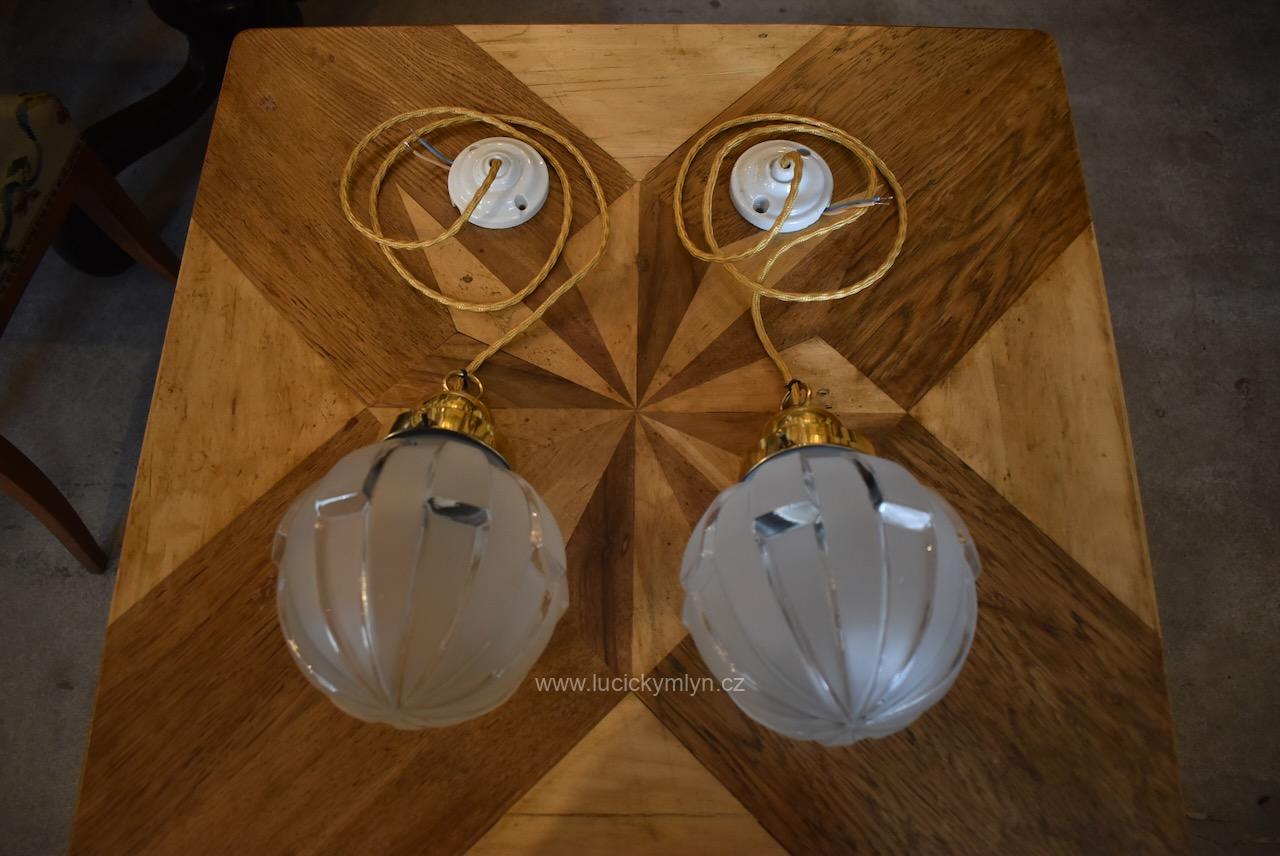 Jednoduchá starožitná párová světla z tlačené a zlatě leštěné mosazi působivě osazená geometricky ztvárněnými skleněnými stínícími koulemi s převážně matným povrchem Starožitná párová závěsná světla z mosazi s geometrickými matovými skleněnými koulemi.
