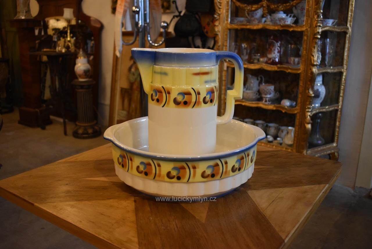 Starožitná toaletní souprava ve stylu ART-DECO – umyvadlo a džbán z krémově bílé keramiky okrášlené stylizovaným geometrickým dekorem ve svěžích tónech žluté, modré a hnědé barvy Starožitná toaletní souprava ART-DECO džbán a lavor se žluto-modro-hnědým geometrickým dekorem