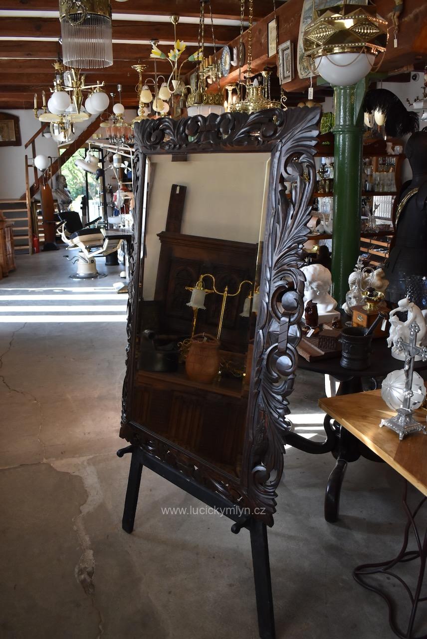 Velké starožitné měšťanské zrcadlo s širokou broušenou fasetou usazené v původním a bohatě řezaném tmavě mořeném dubovém rámu působivě provedeném v okázalém neorenesančním stylu ze 3. 1/3 19. stol. Velké starožitné měšťanské zrcadlo v neorenesančním tmavě mořeném dubovém rámu s fazetou.
