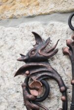 Starožitný ručně kovaný nástěnný věšáček ve tvaru renesanční mříže s hlavičkami dráčků.