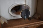 Starožitné prvorepublikové nástěnné kuchyňské hodiny s bílým porcelánovým čílkem a kyvadlem.