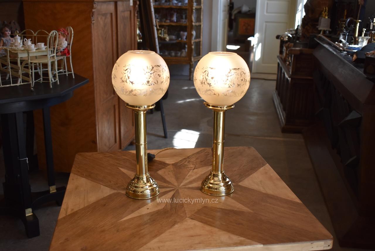 Okouzlující pár starožitných stolních lamp z tlačené mosazi osazených původními stínícími koulemi vše ze závěru 19. stol. původně konstruované na vsazené voskové svíce posouvané do horní polohy vinutou pružinou - nyní šikovně elektrifikováno za použití prvorepublikových objímek na šroubovací žárovku Starožitné párové mosazné stolní lampy se skleněnými koulemi, elektrifikované, závěr 19. stol.