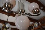 Starožitný funkcionalistický tří-ramenný chromovaný lustr s mléčně narůžovělými skleněnými koulemi.