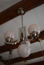 Starožitný funkcionalistický tří-ramenný chromovaný lustr s mléčně narůžovělými skleněnými koulemi.