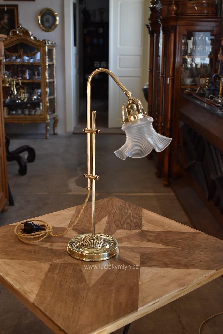 Vyšší starožitná stolní lampa vyrobená z leštěné mosazi v secesním stylu má stabilní a těžkou podstavu i elegantní, výškově posuvné obloukové rameno nenápadně zakončené směrově nastavitelným kloubem s upínacím košíčkem ručně foukaného stínidla Starožitná secesní mosazná stolní lampa s posuvným ramenem a foukaným stínidlem ve tvaru květu.