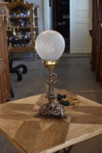 Starožitná stolní lampa z patinované litiny s lvími maskami a broušenou skleněnou koulí.