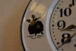 Starožitné kuchyňské hodiny s oválným porcelánovým ciferníkem a rokokovými stínovými postavičkami.
