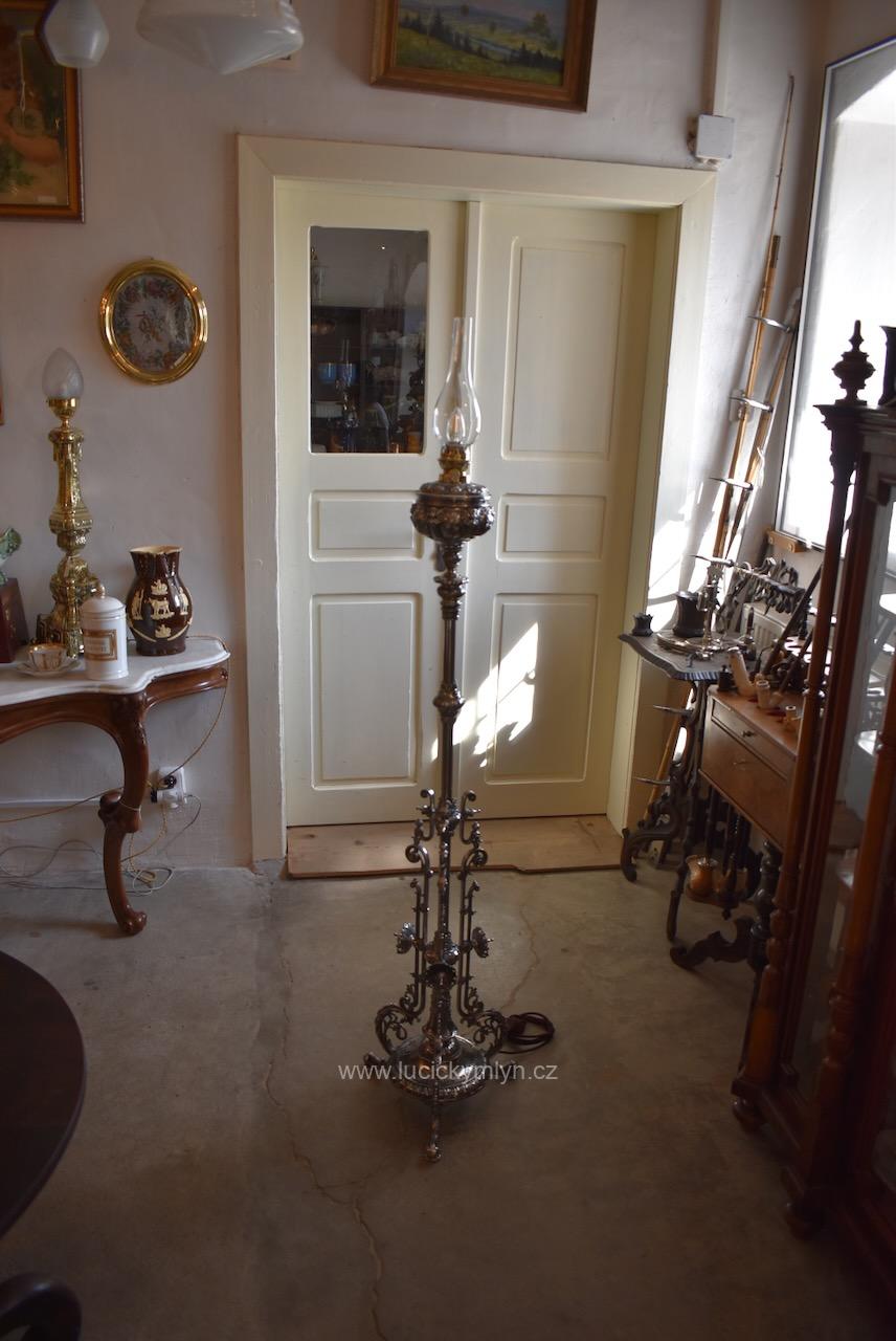 Ojedinělá a vysoká starožitná stojací lampa z umělecké stříbrně niklované litiny okázale ztvárněná v historizujícím stylu šikovně a nenápadně upravená z klasické petrolejové lampy na praktické a reprezentativní elektrické osvětlení Starožitná stojací lampa z niklované litiny, elektrifikovaná z petrolejky, do roku 1900.