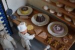 Starožitné diorama historické pekárny s kachlovou pecí a figurkami pekařů.
