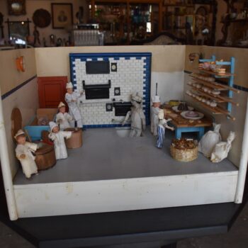 Starožitné diorama historické pekárny s kachlovou pecí a figurkami pekařů.