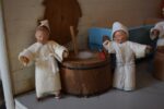 Starožitné diorama historické pekárny s kachlovou pecí a figurkami pekařů.