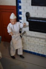 Starožitné diorama historické pekárny s kachlovou pecí a figurkami pekařů.