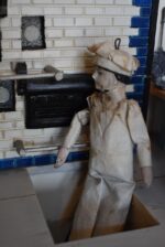 Starožitné diorama historické pekárny s kachlovou pecí a figurkami pekařů.