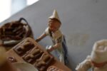 Starožitné diorama historické pekárny s kachlovou pecí a figurkami pekařů.