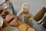 Starožitné diorama historické pekárny s kachlovou pecí a figurkami pekařů.