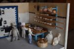 Starožitné diorama historické pekárny s kachlovou pecí a figurkami pekařů.