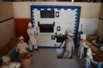 Starožitné diorama historické pekárny s kachlovou pecí a figurkami pekařů.