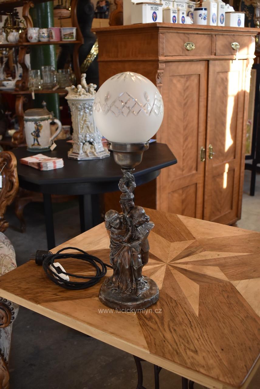 Vyšší starožitná figurální romanticky pojatá lampička se sloupkem půvabně oživeným zámeckými postavičkami mladého páru a na vrcholu osazená upínacím kloboučkem se stínícím broušeným sklem (Kopírovat) Starožitná figurální lampička s postavičkami mladého páru a broušenou skleněnou koulí.