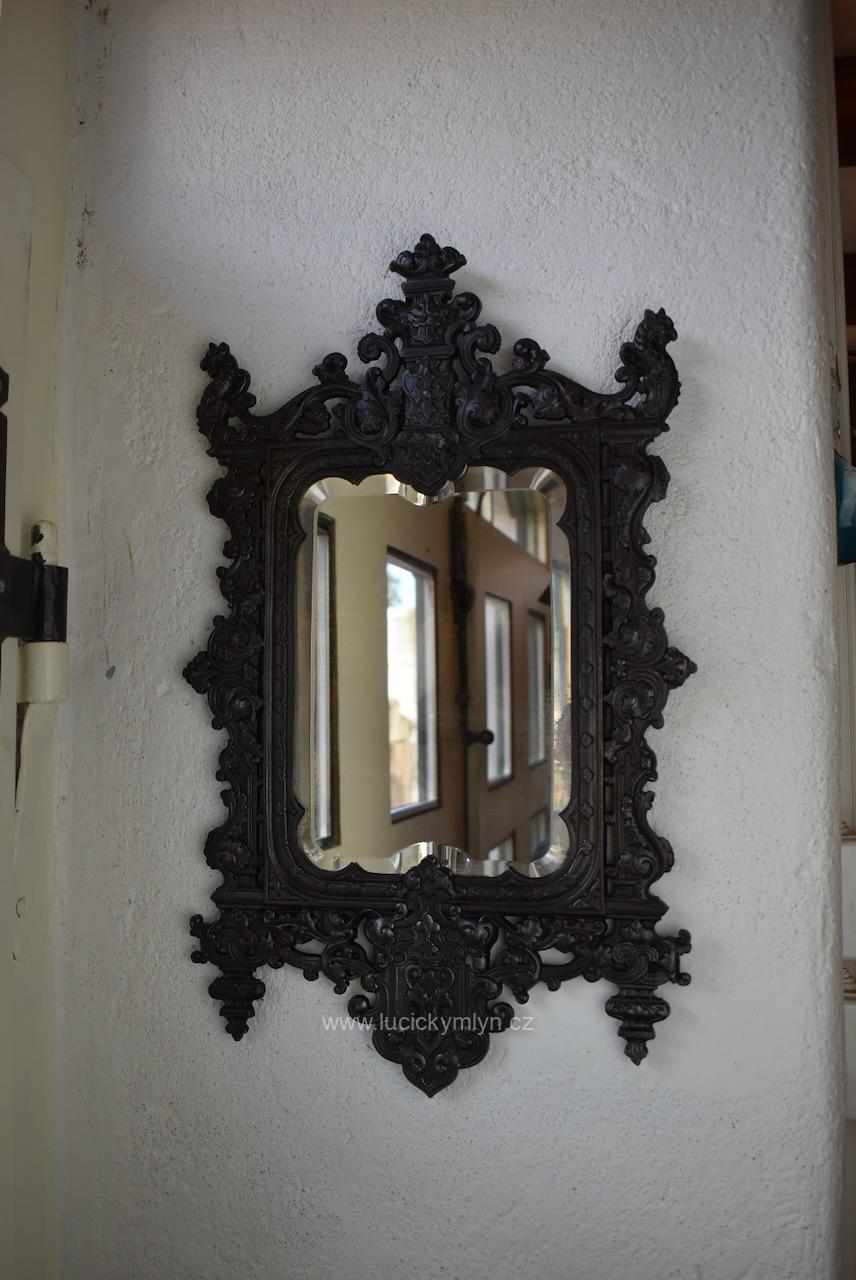 Starožitné závěsné zrcadlo v bohatě propracovaném rámu z umělecké litiny okrášlené prokrajovanými rostlinnými ornamenty kartušemi a stylizovanými zvířecími motivy osazené originál. fazetovým sklem Starožitné závěsné zrcadlo v neorenesančním litinovém rámu s fazetovým sklem.