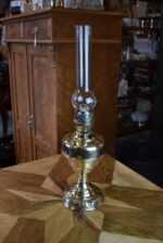 Starožitná mosazná petrolejová lampa ve tvaru poháru se skleněným cylindrem z okolo roku 1910.