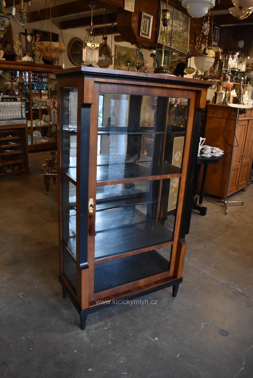 Vkusný starožitný třešňový skleník z bohatšího měšťanského prostředí vyrobený do r. 1830 ve stylu biedermeier jež charakterizují štíhlé jehlové nohy ušlechtilé ovocné dřevo kombinované s ebenově černými dílci (Kopírovat) Starožitný biedermeierovský třešňový skleník z období do roku 1830.